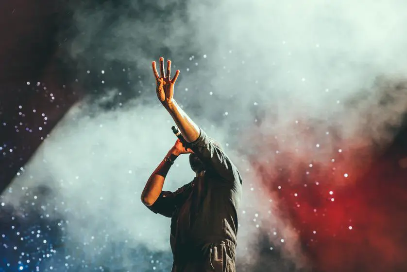 Un chanteur sur scène qui lève la main gauche en l'air et qui est devant un nuage de fumée